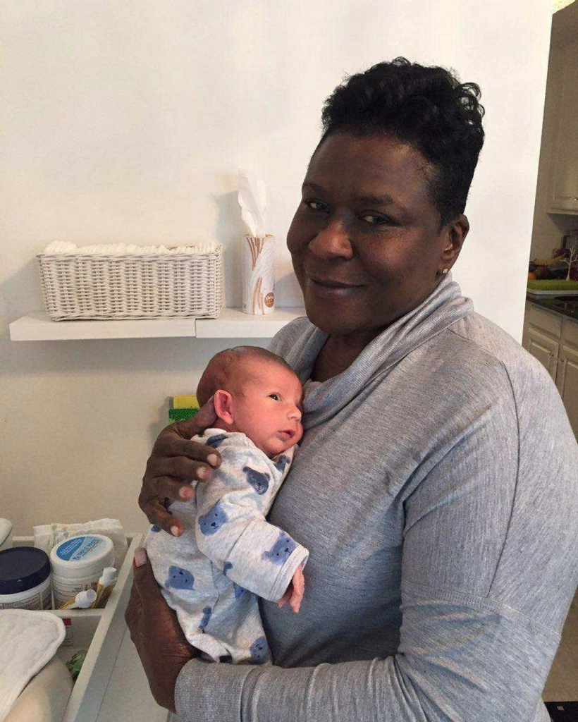 Postpartum Doula holding newborn baby boy smiling.