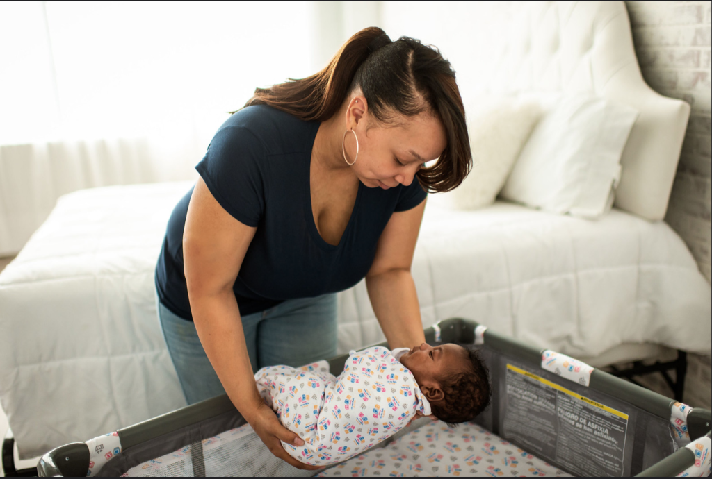 Mom placing baby safely to sleep on a firm flat mattress. 