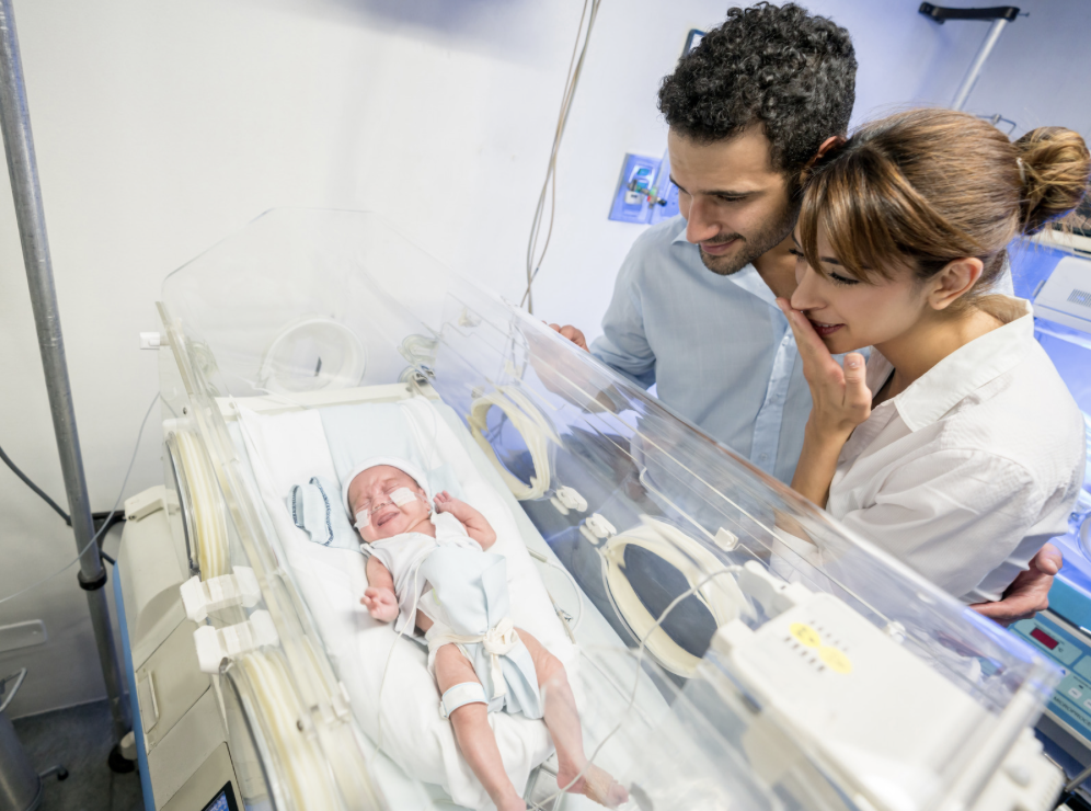Parents bringing baby home the NICU looking at baby in hospital Isolette.